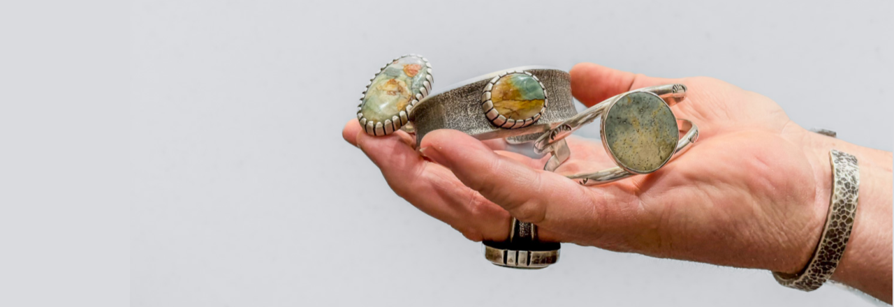 Hand holding a silver bracelet with gemstones against a light gray background